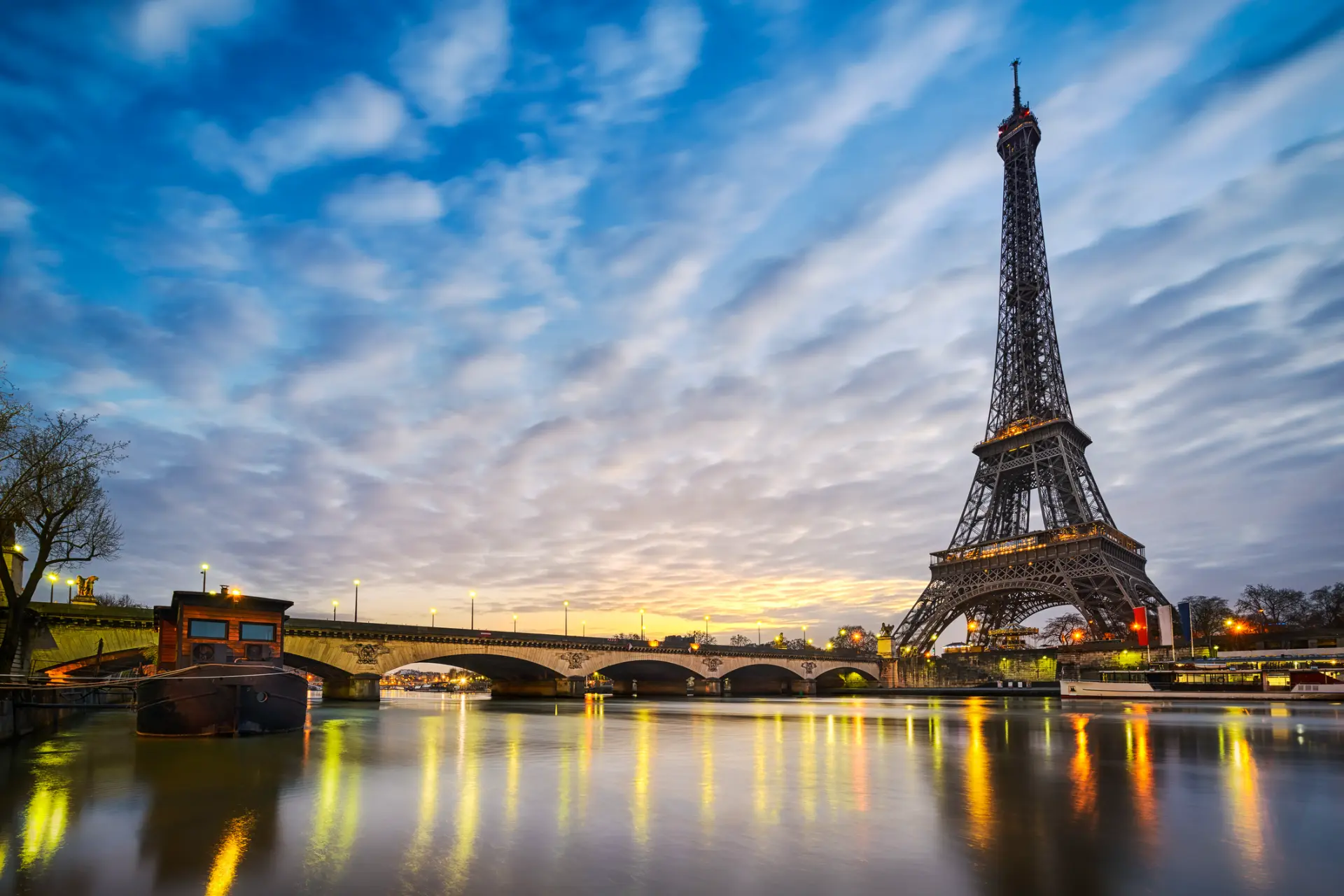 The Eiffel Tower at dusk seen across the Seine with city lights reflecting on the water